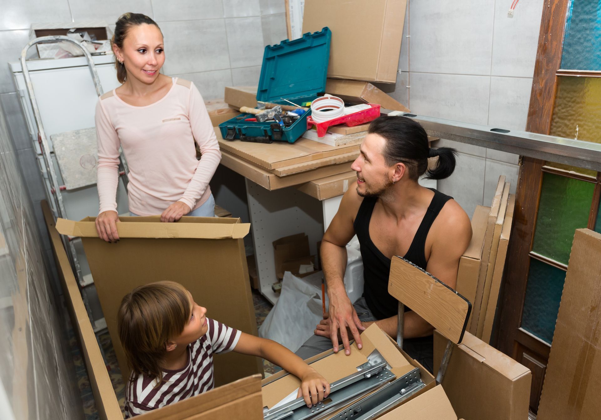 A man , woman and child are sitting in cardboard boxes in a room.