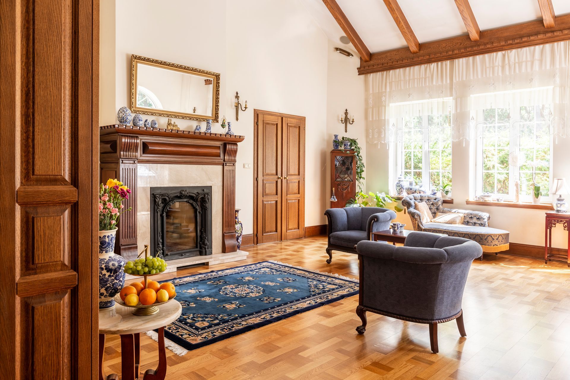 Elegant living room with fireplace, blue rug, armchairs, and light-filled windows.