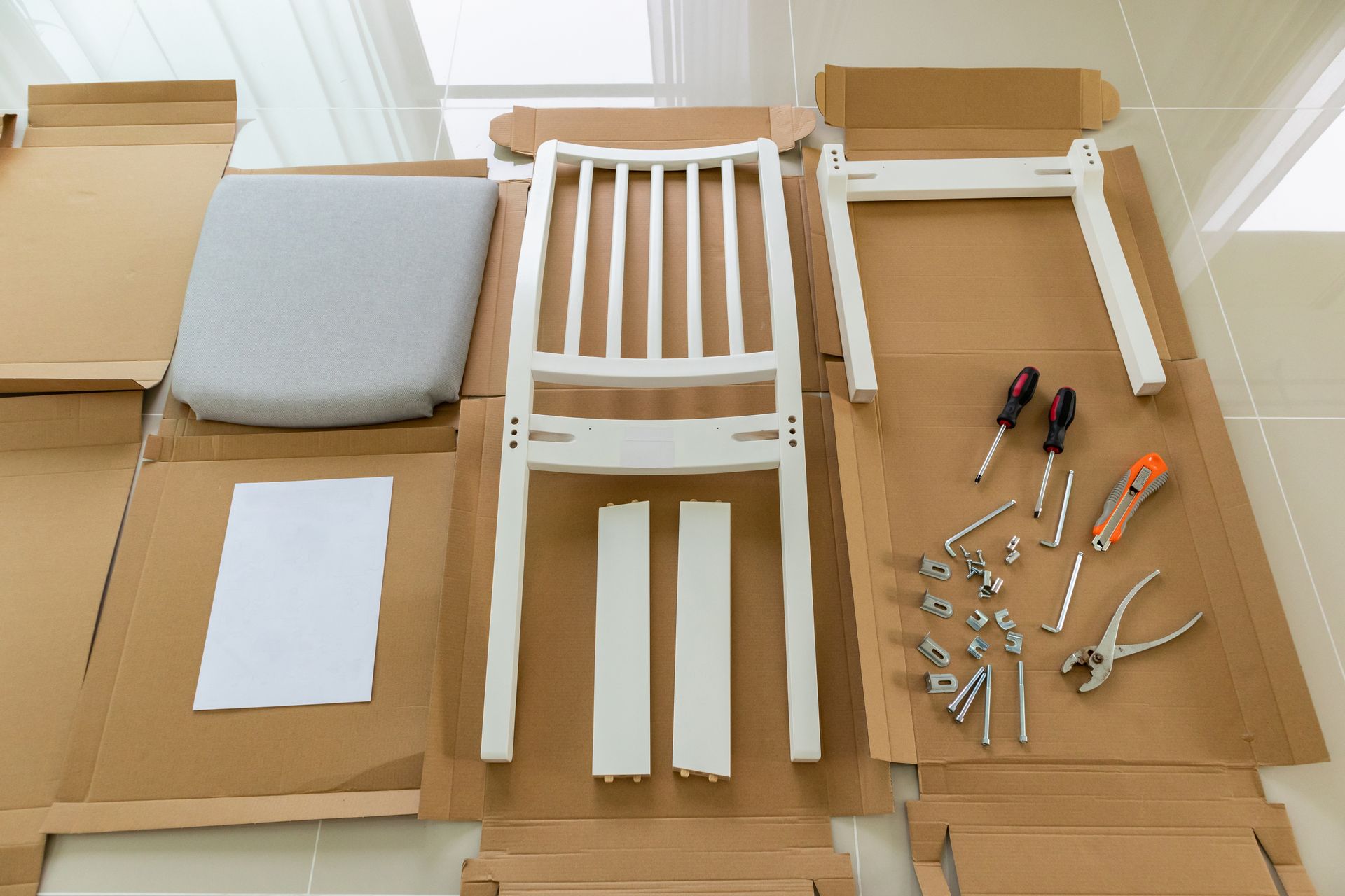Disassembled white chair components on cardboard, with tools and hardware, ready for assembly.