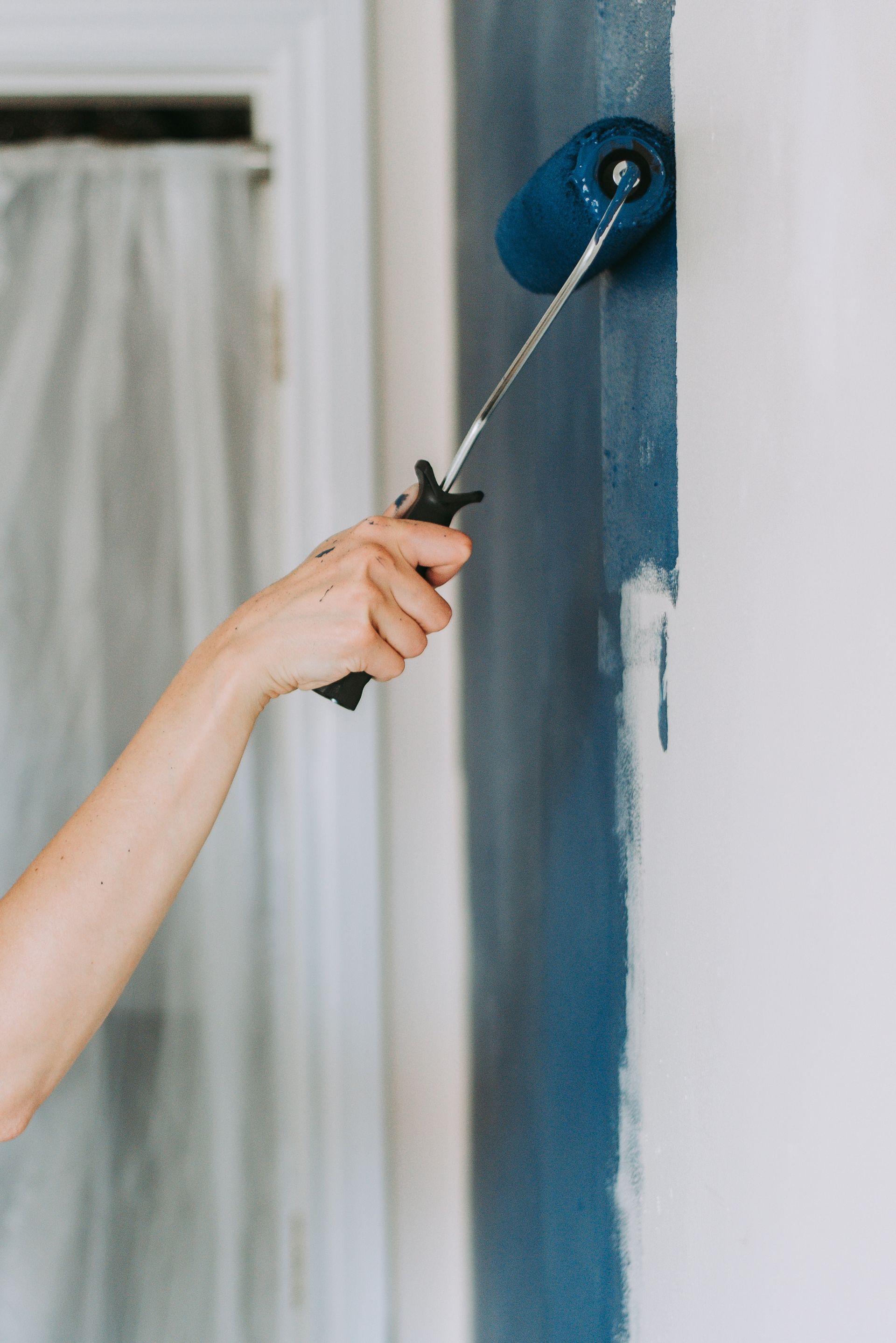 A person is painting a wall with a blue paint roller.