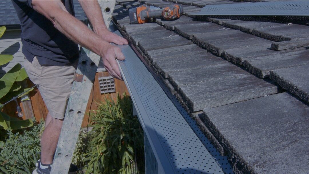 A close up of a gutter with leaves on it and a roof in the background.