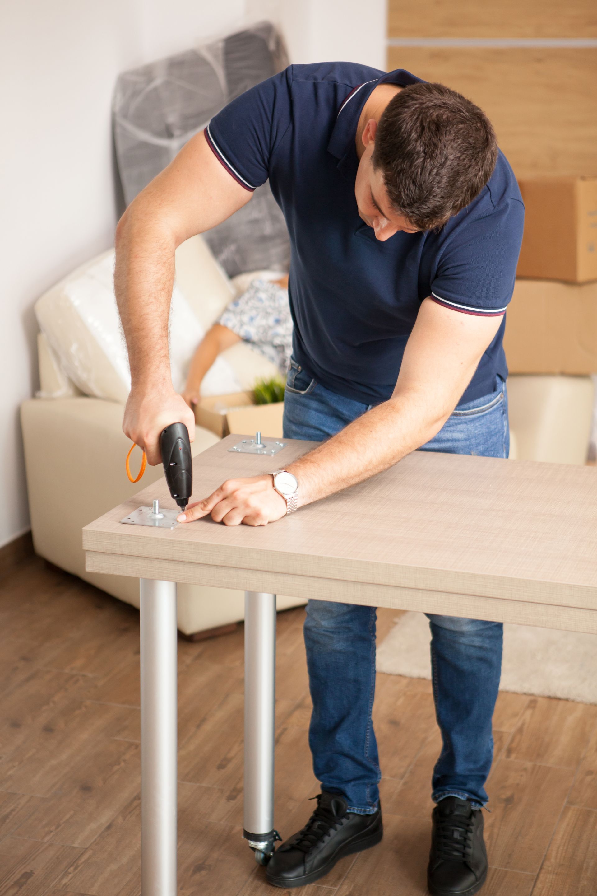 A man is using a drill to fix a table in a living room.