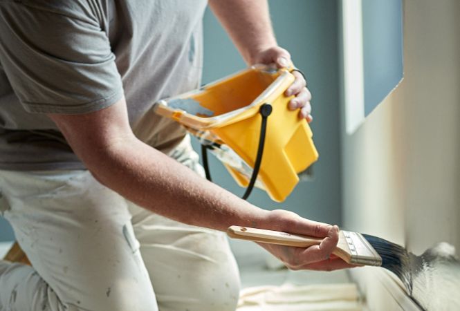 A man is painting a black ceiling with a roller.