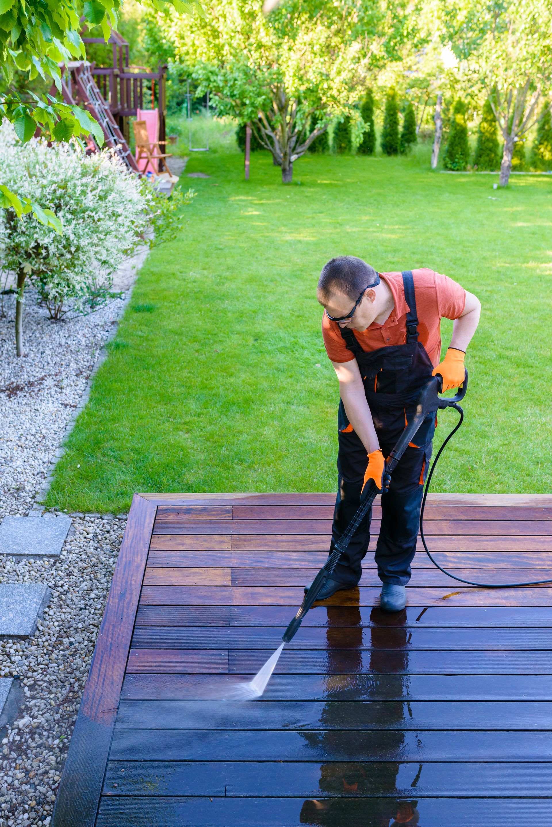 A man is cleaning a wooden deck with a high pressure washer.