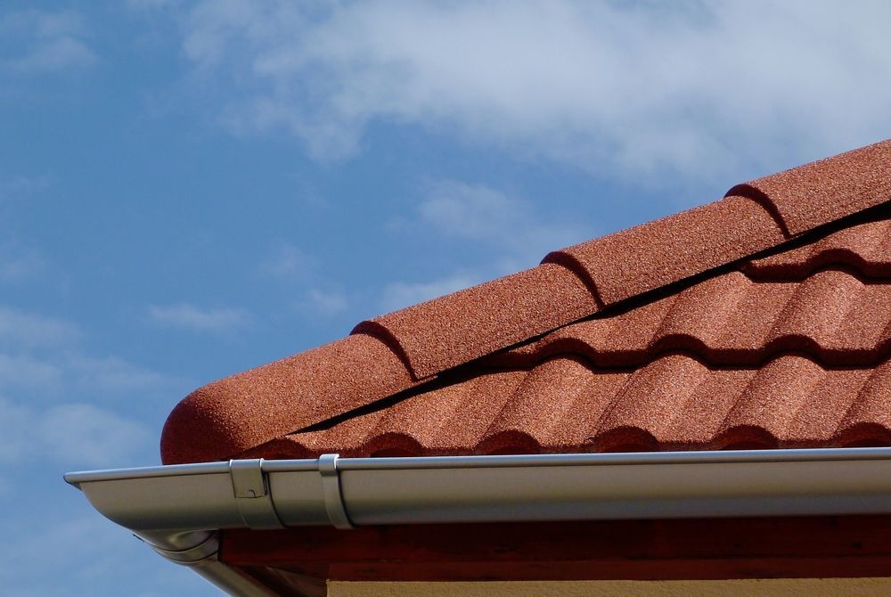 A red tile roof with a white gutter and a blue sky in the background