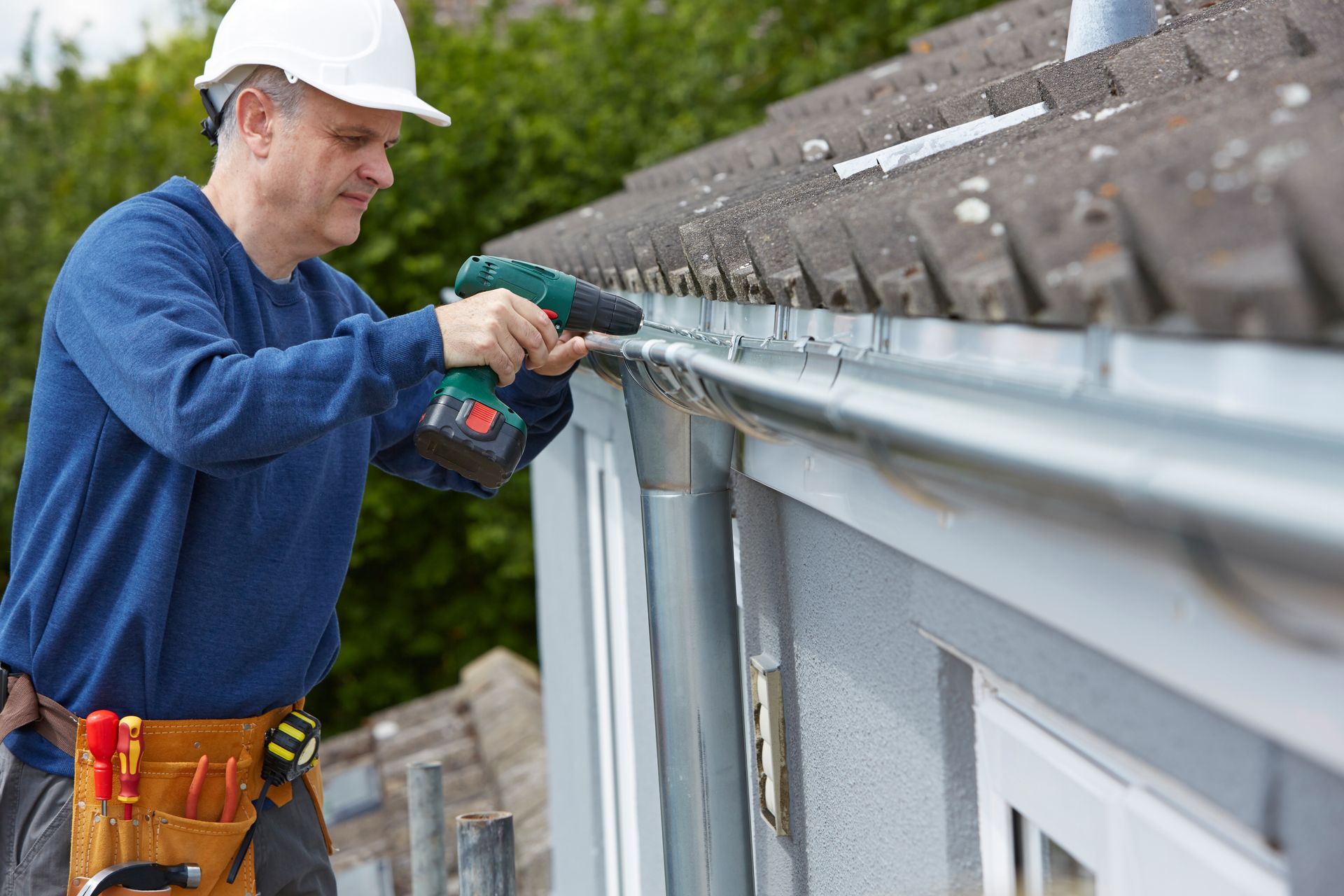 A man is installing a gutter on the side of a house.