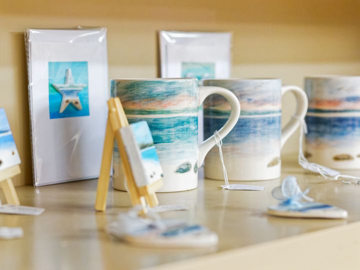 A shelf with mugs and paintings on it