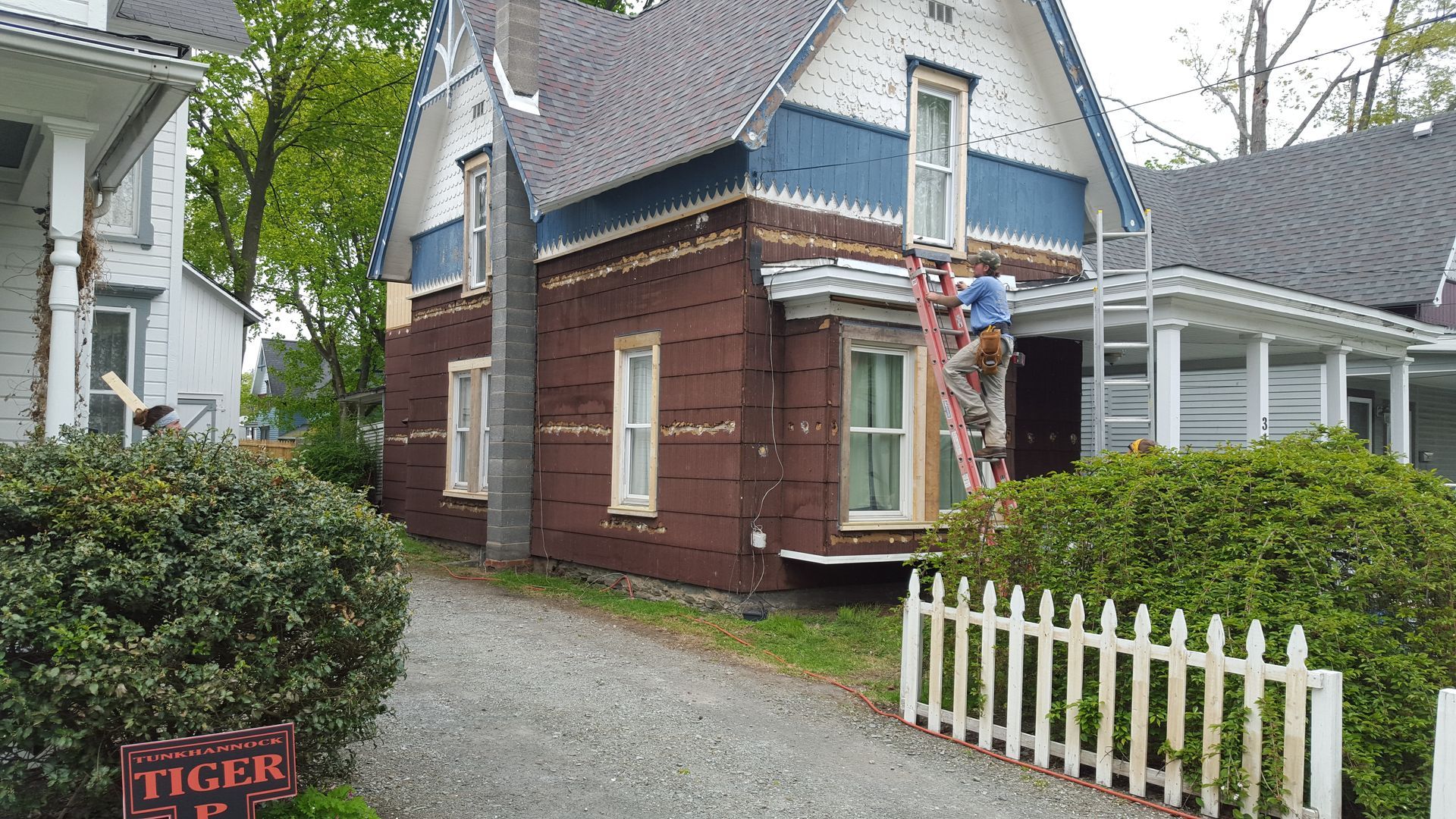 A man on a ladder is painting the side of a house.
