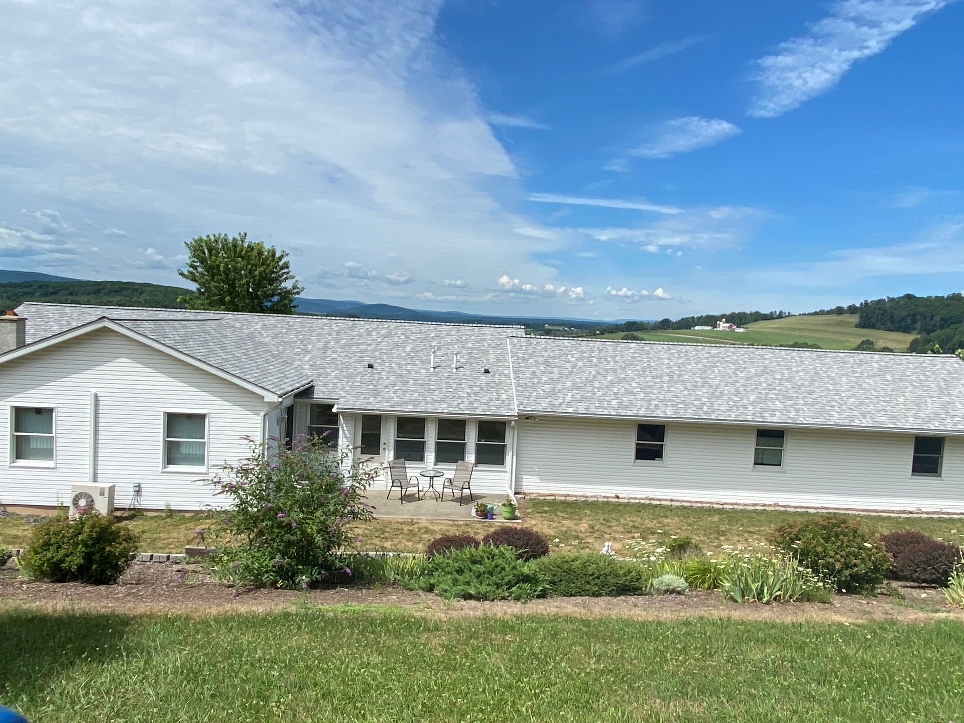 A large white house with a gray roof sits in the middle of a grassy field