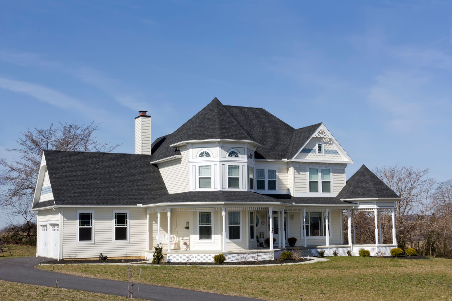 A large white house with a black roof is sitting on top of a lush green field.