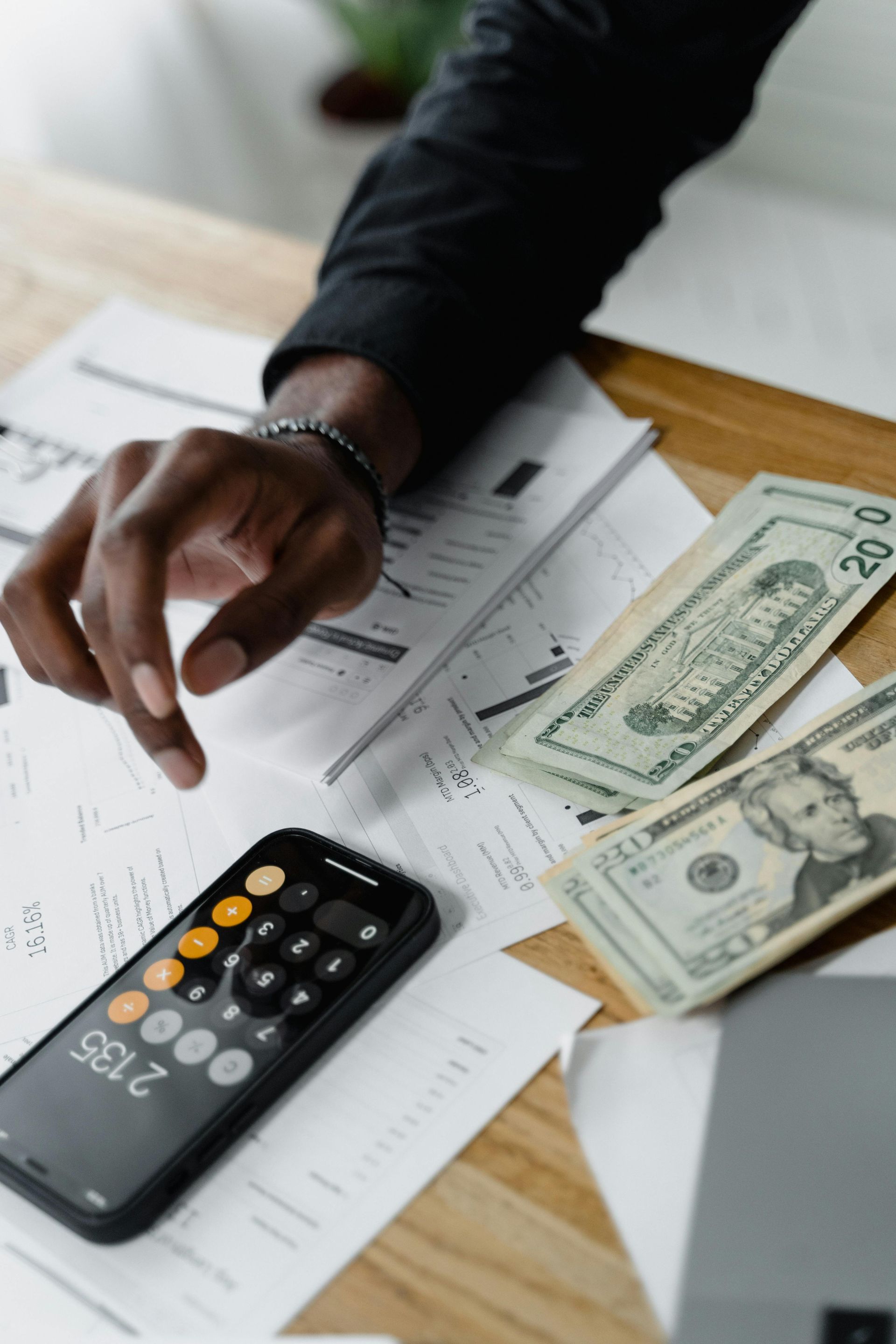 A person is using a calculator on a table with money and papers.