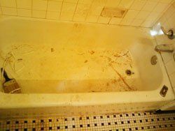 A dirty bathtub in a bathroom with a tiled floor.