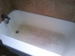 A dirty bathtub in a bathroom with a tiled wall.
