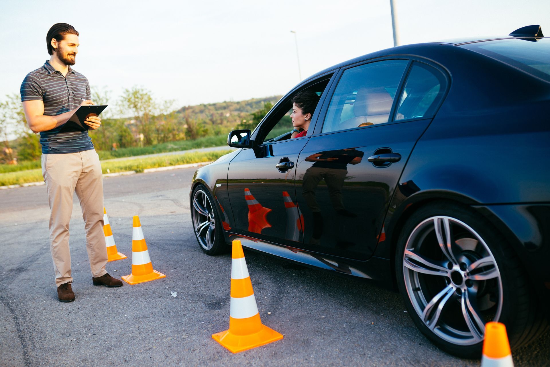 Driving lesson: Instructor observes driver maneuvering car around orange traffic cones.