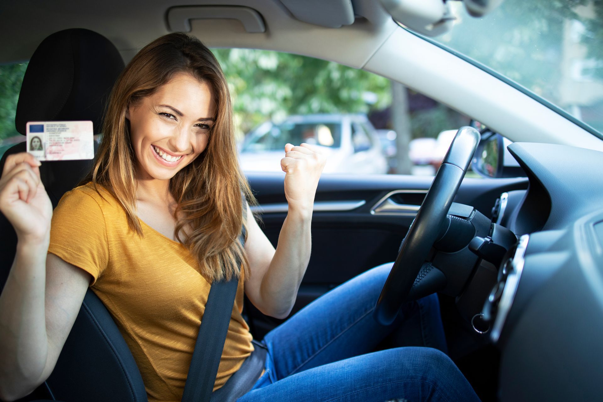 Woman in car, holding a driver's license, smiling.