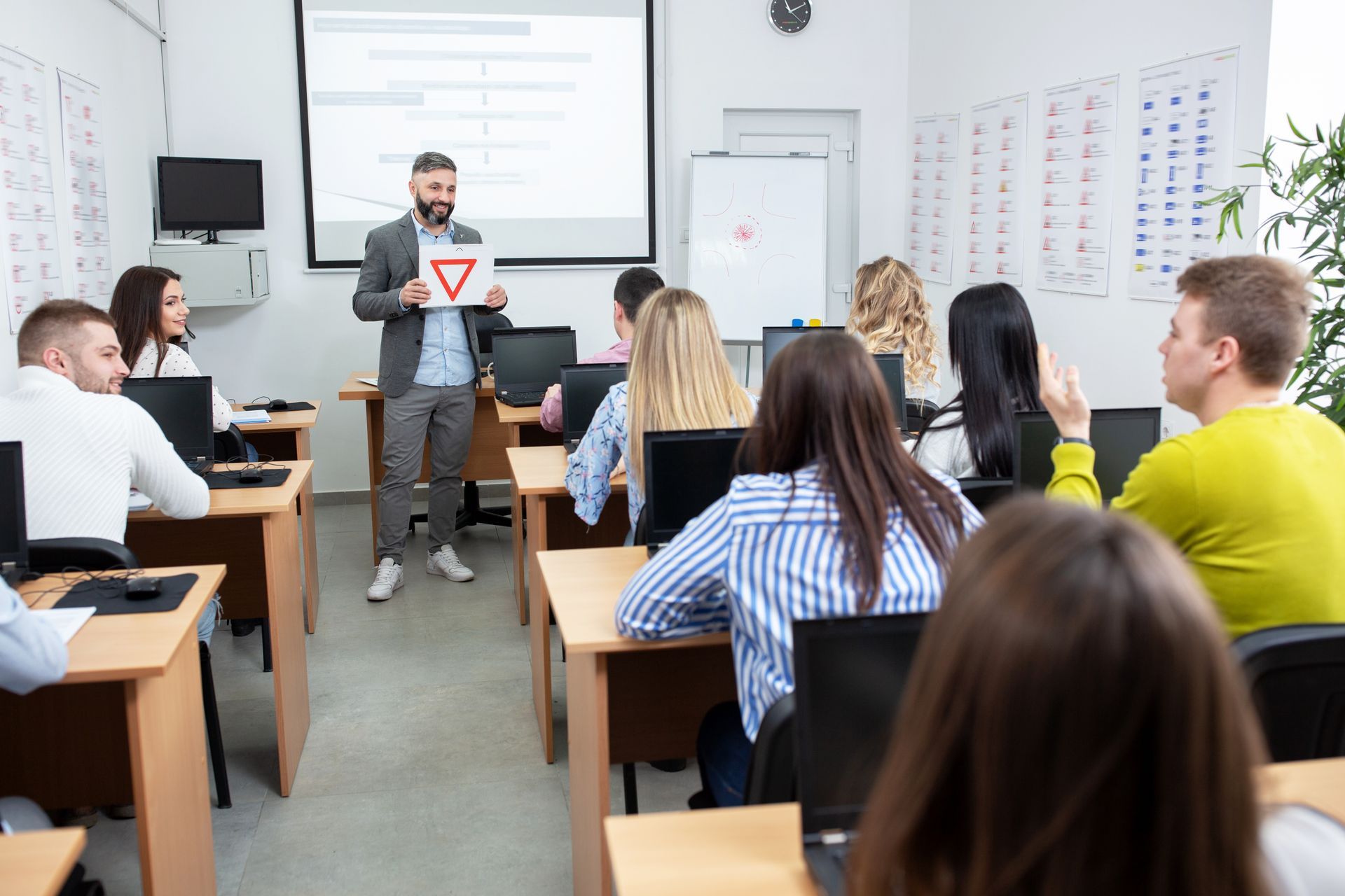 Driving instructor teaching students in a classroom, holding a yield sign.