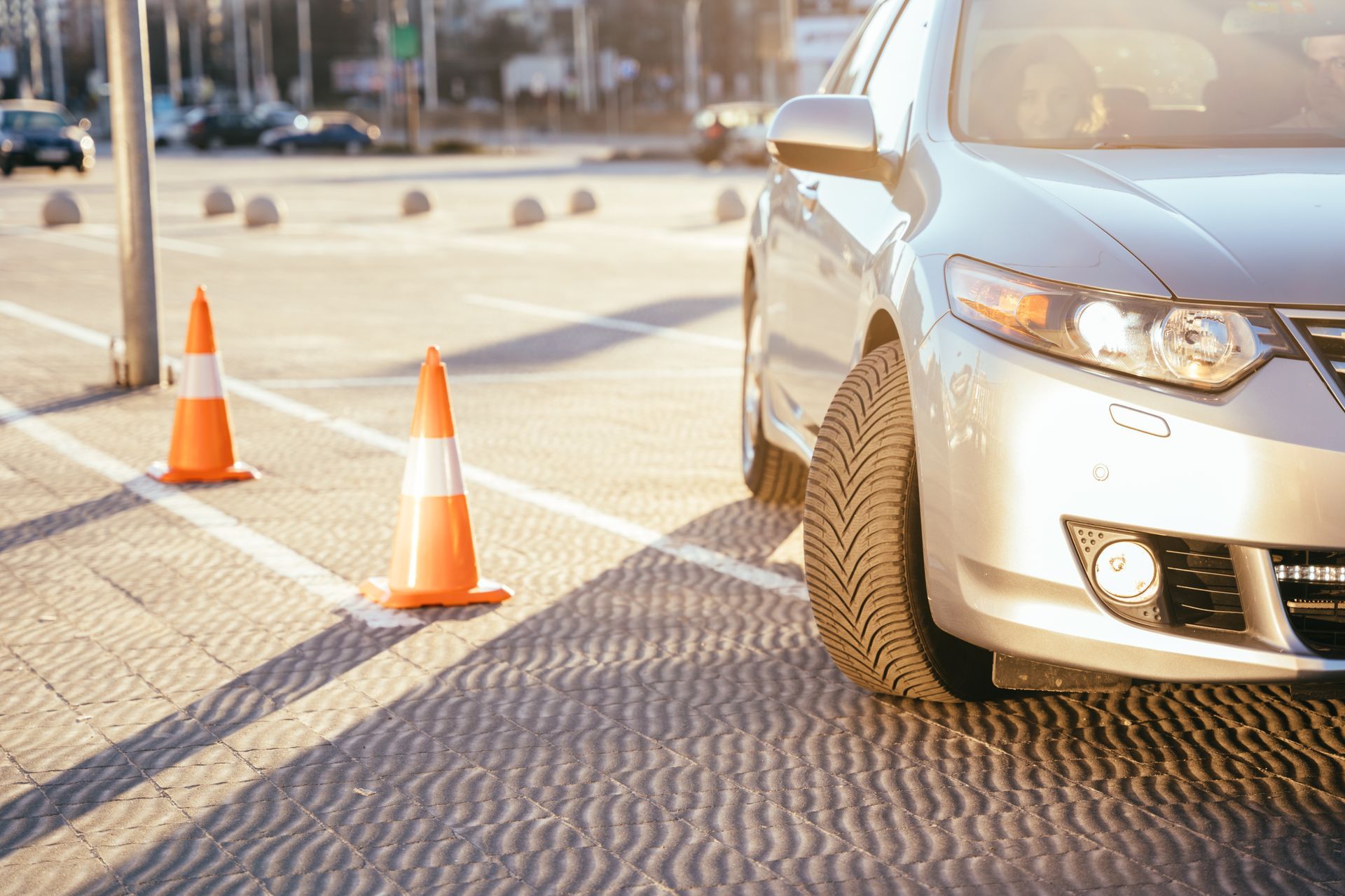 Silver car parked near two orange traffic cones in a paved lot.