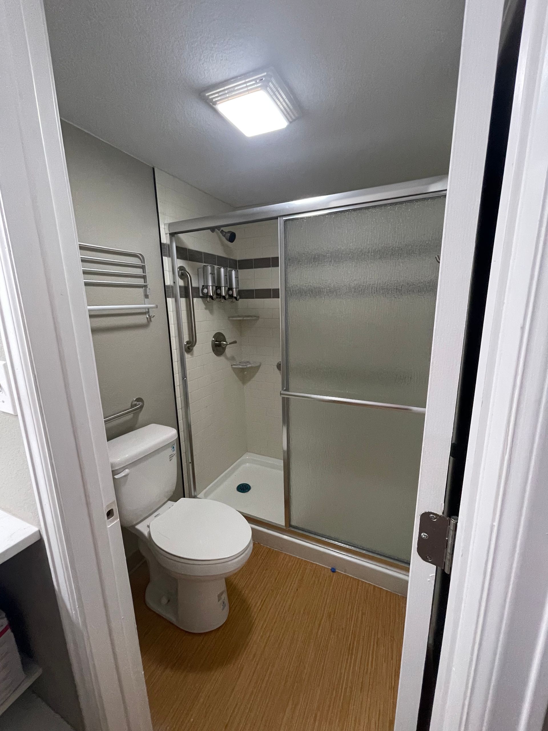Small bathroom with a toilet, shower, and a towel rack; beige flooring, white walls.
