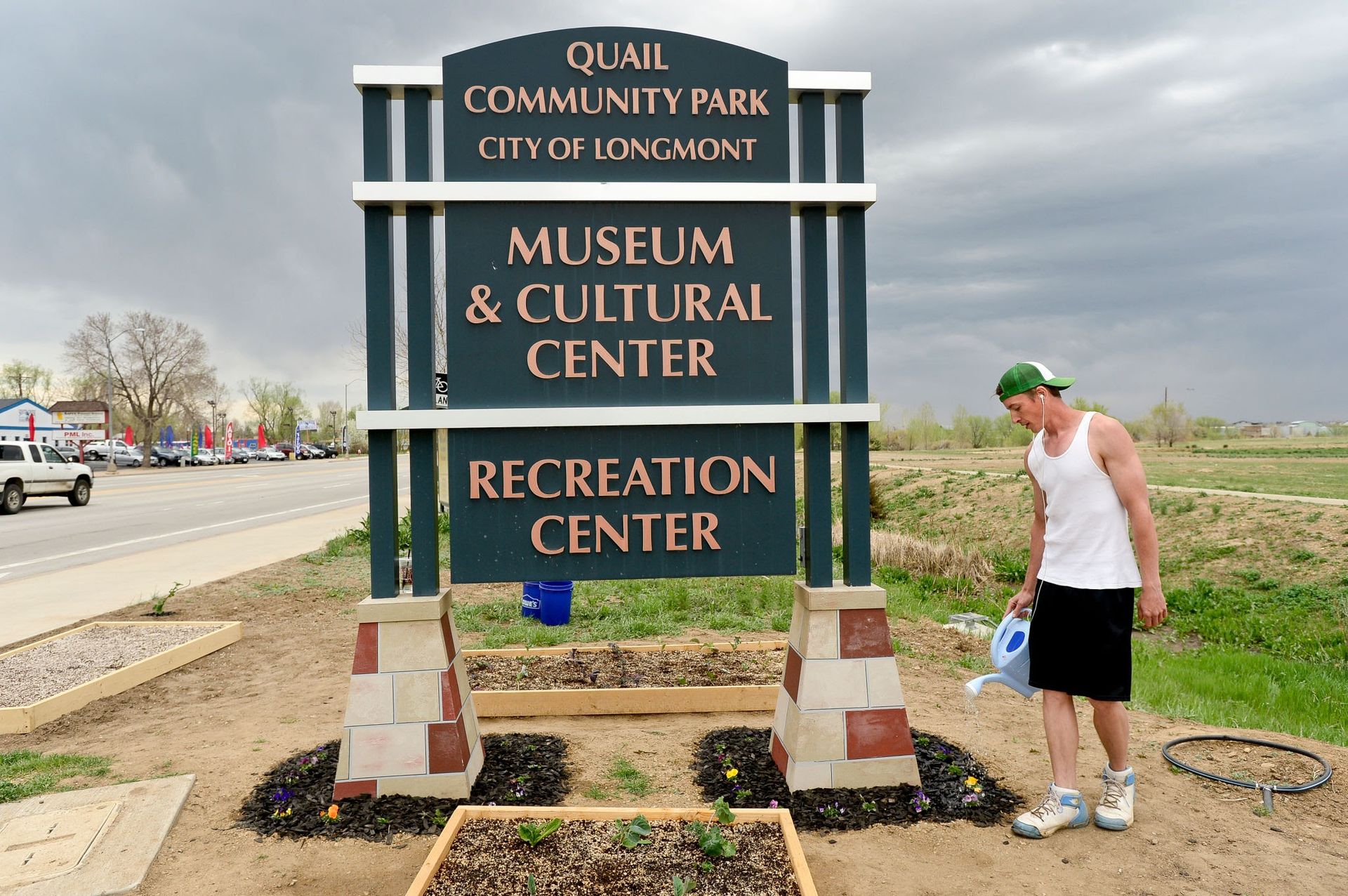 Man waters flowers near a sign for Quail Community Park in Longmont, Colorado.