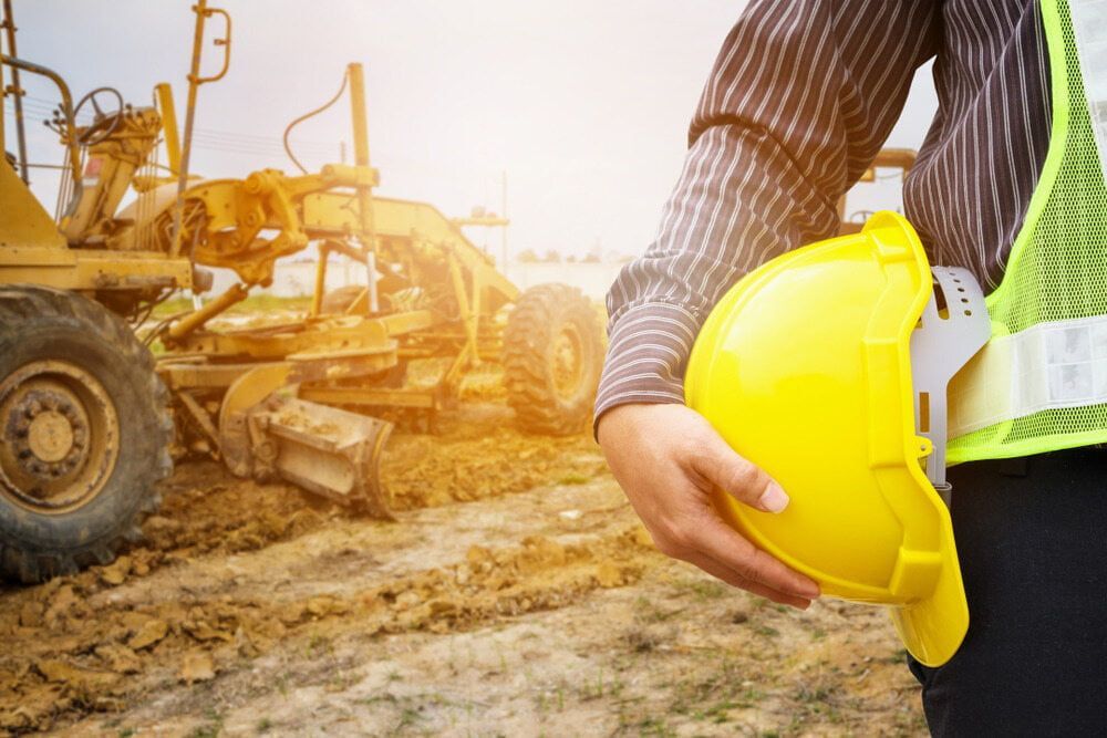 A Construction Worker is Holding a Yellow Hard Hat at a Construction Site — Calibre Resourcing Solutions in Mount Isa City, QLD