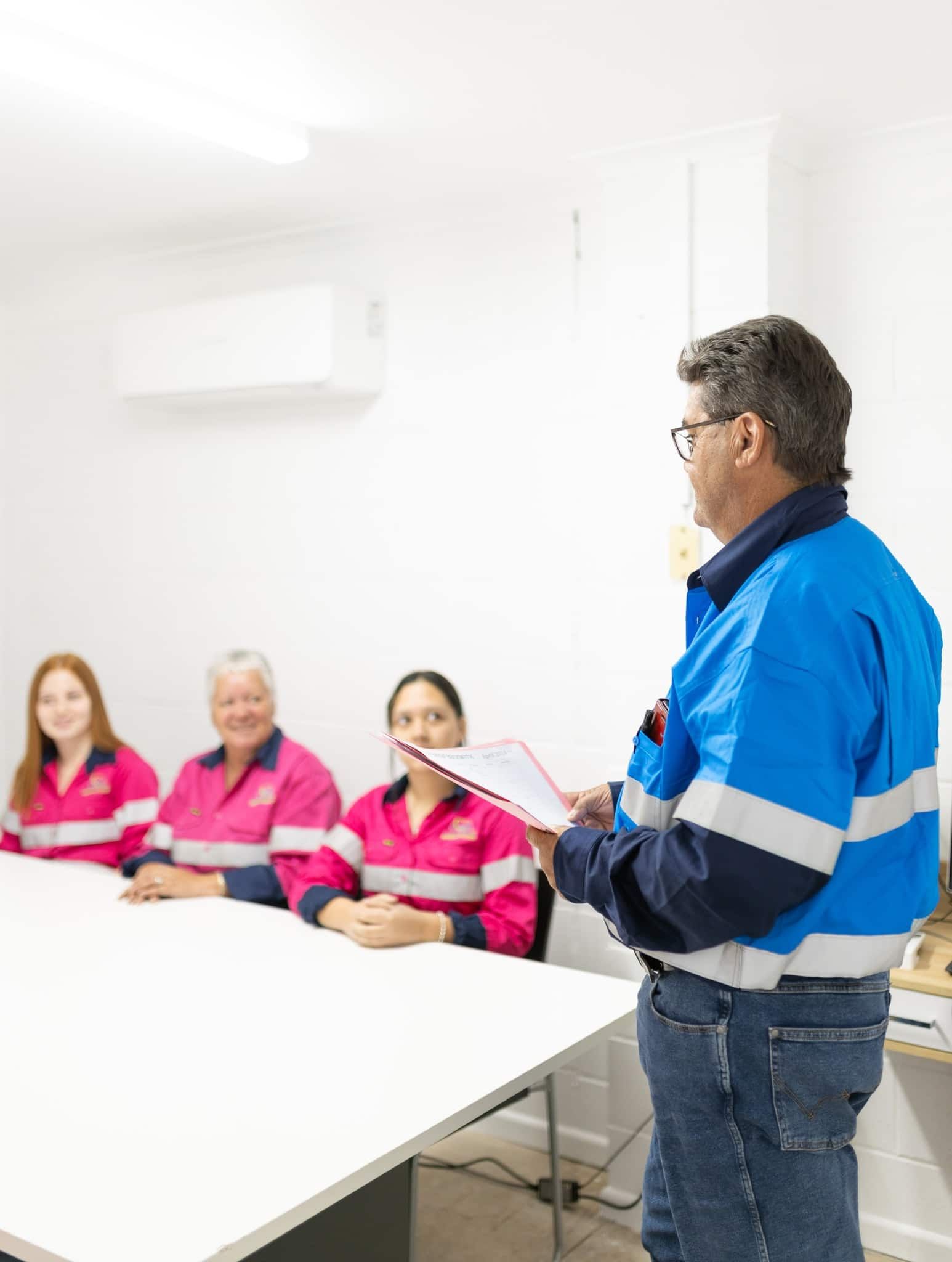 A Man in a Blue Jacket is Giving a Presentation to a Group of People Sitting at a Table — Calibre Resourcing Solutions in Townsville, QLD