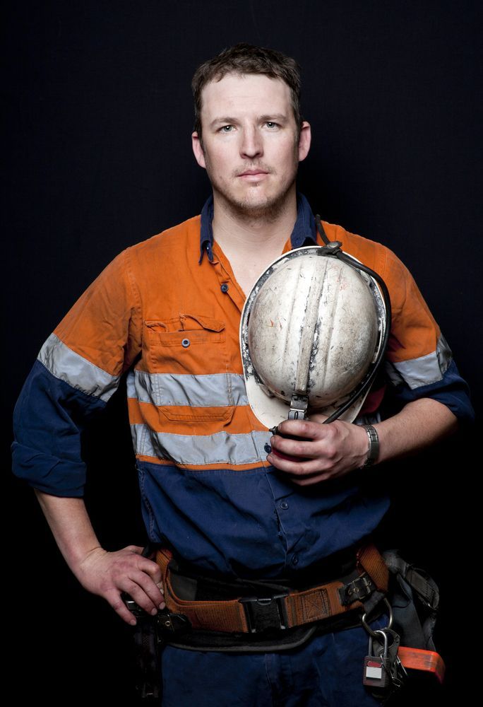 A Man in an Orange and Blue Shirt is Holding a Hard Hat — Calibre Resourcing Solutions in Cairns, QLD