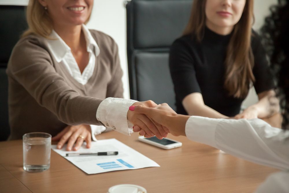A Woman is Shaking Hands With Another Woman at a Table — Calibre Resourcing Solutions in Mount Isa City, QLD