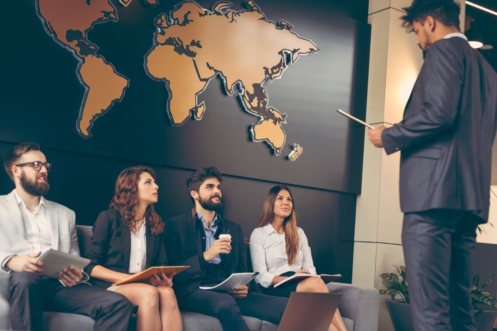 A Group of Business People Are Sitting on a Couch in Front of a Map of the World — Calibre Resourcing Solutions in Gladstone, QLD