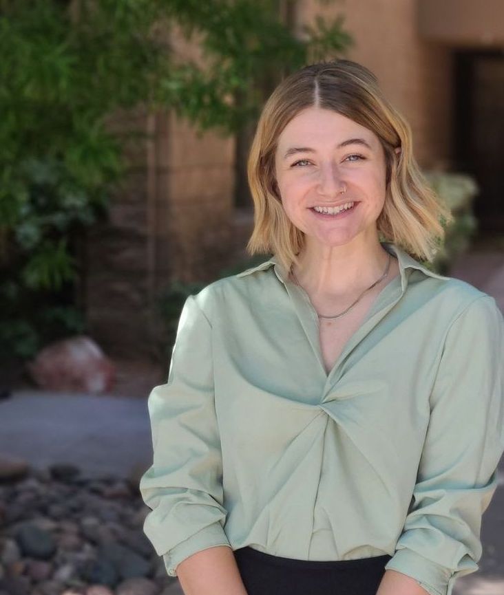 A woman in a green shirt is smiling with her arms crossed.