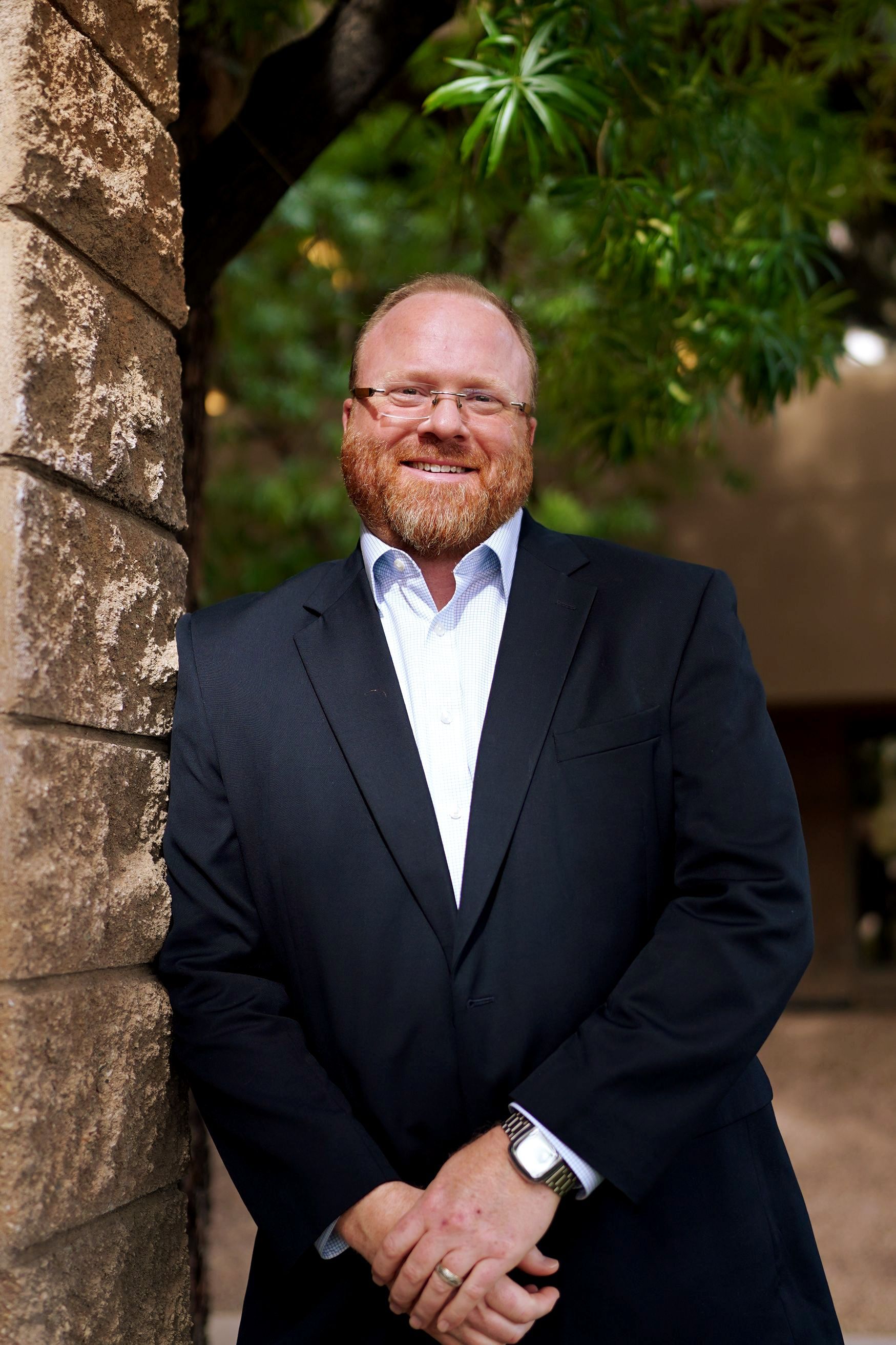 A man in a suit and white shirt is leaning against a brick wall.