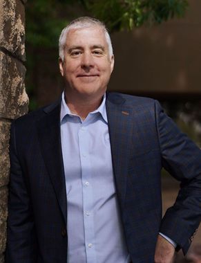 A man in a suit and shirt is leaning against a stone wall.