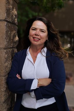 A woman is leaning against a stone wall with her arms crossed.