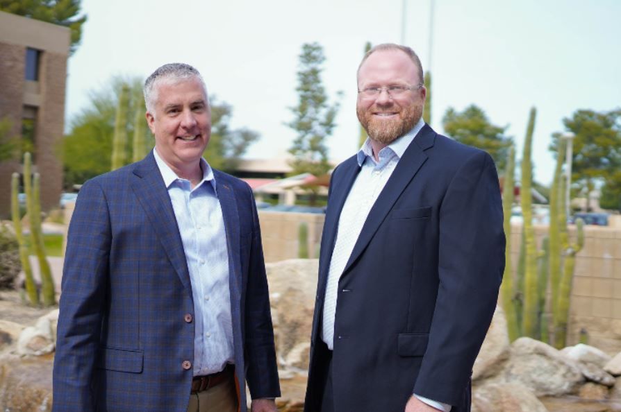 Two men in suits are standing next to each other in front of a cactus garden.