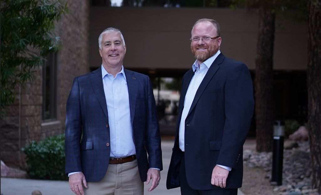 Two men in suits are standing next to each other in front of a building.