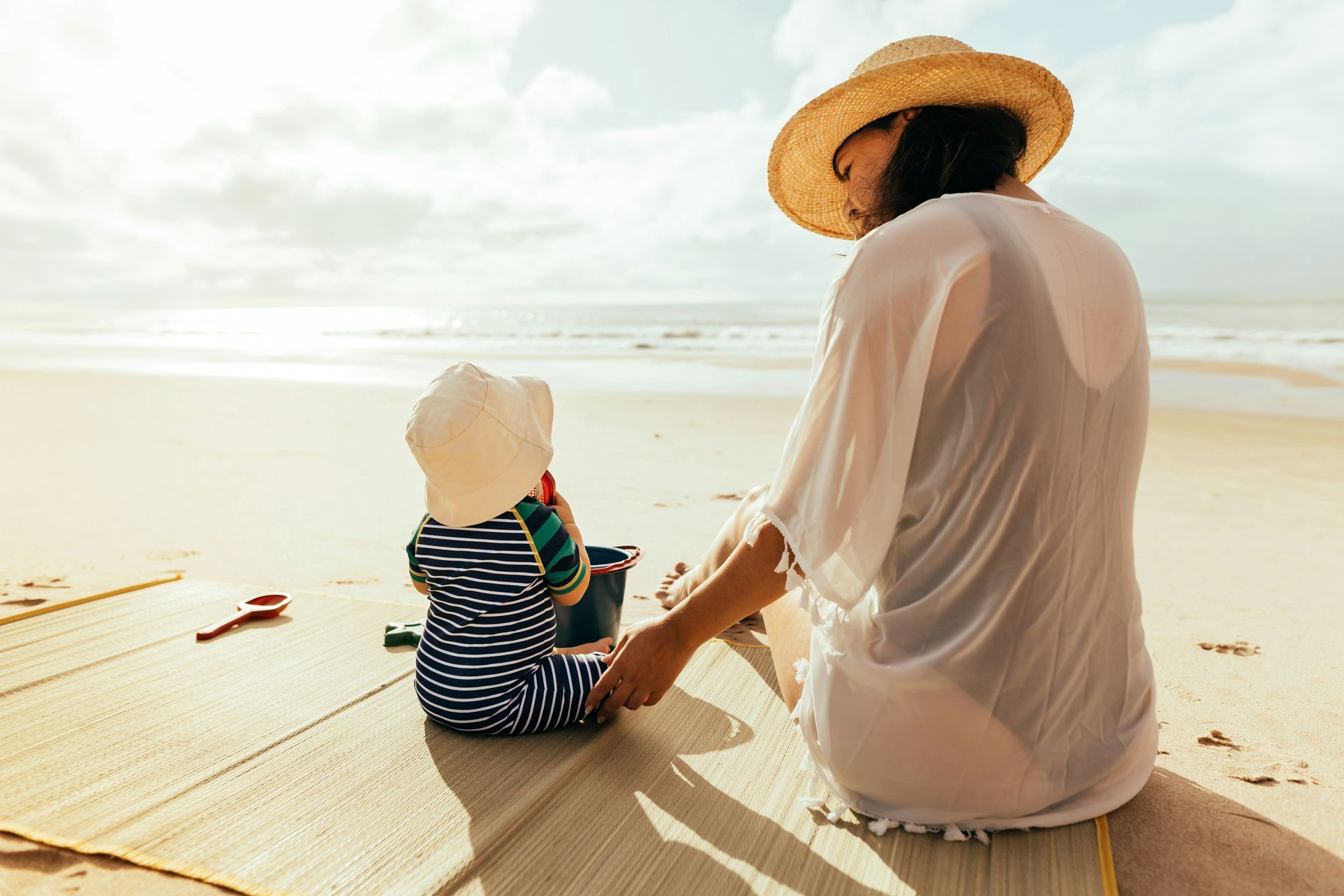 A woman and a baby are sitting on the beach looking at the ocean.