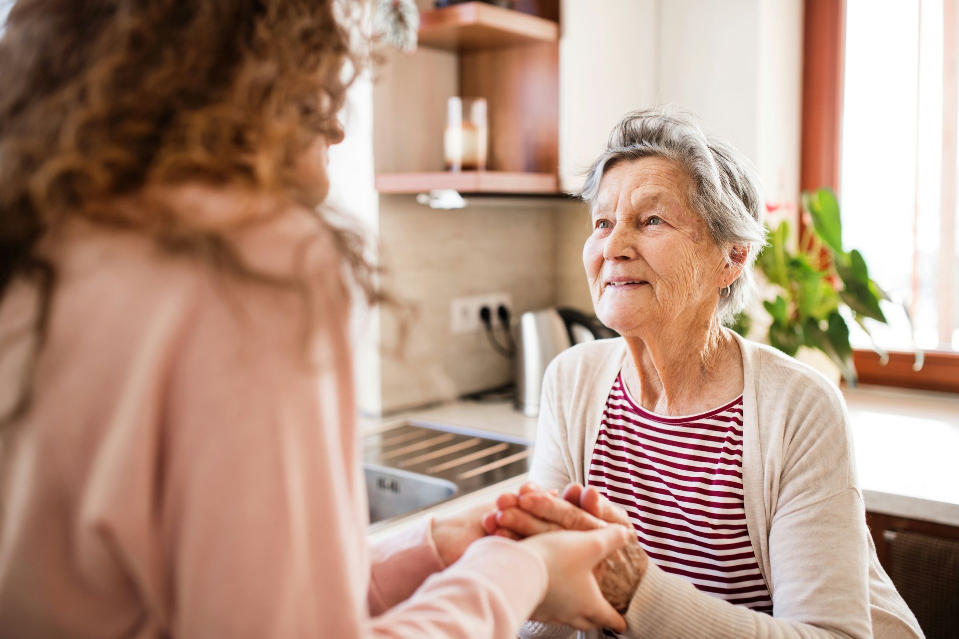 A woman is holding the hands of an elderly woman in a kitchen.