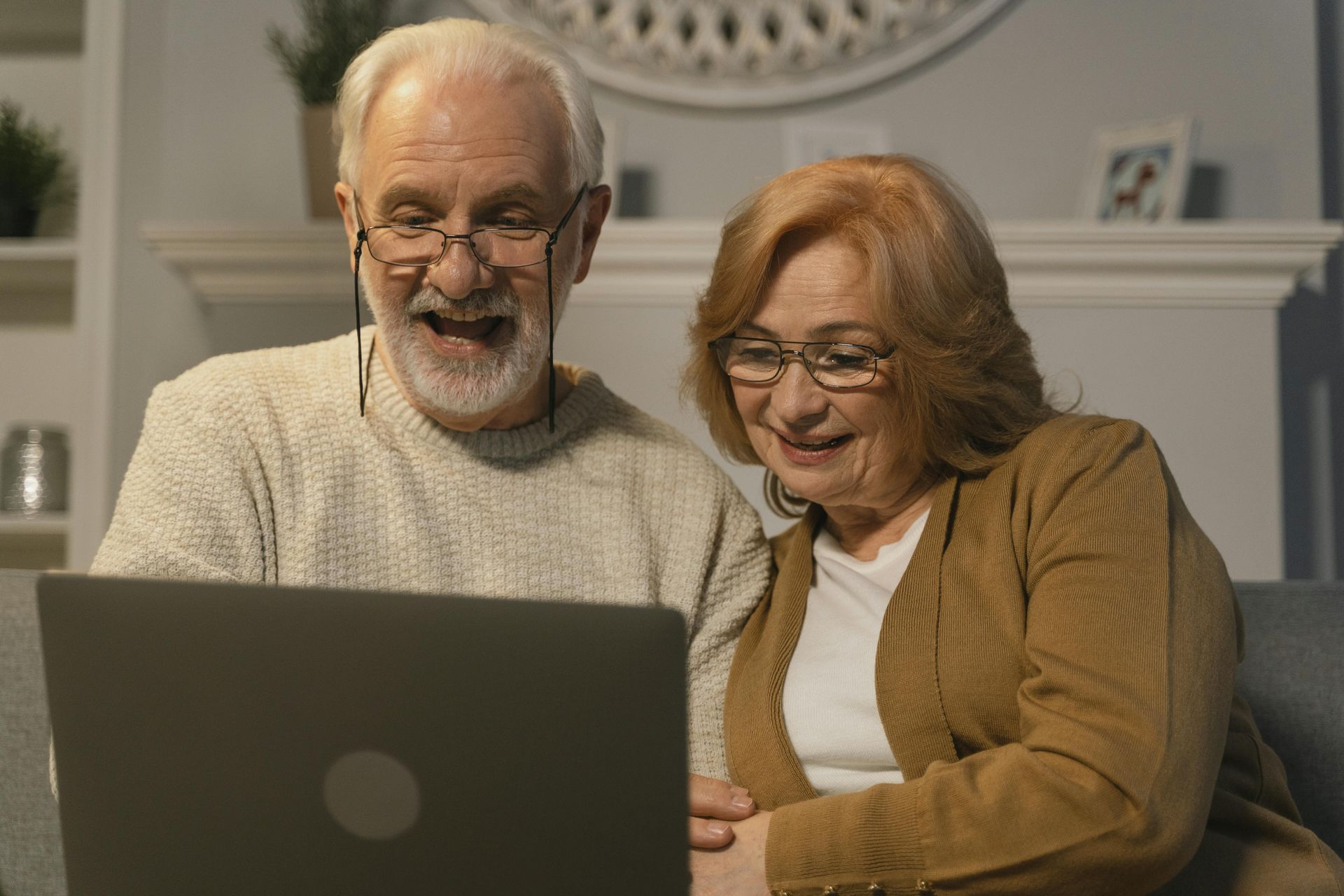 An elderly couple is sitting on a couch looking at a laptop computer.
