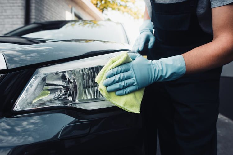 A person is cleaning the headlight of a car with a microfibre cloth.