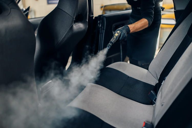 A person is cleaning the seats of a car with a steam cleaner.
