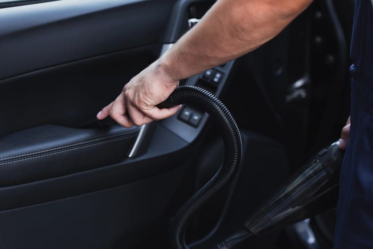 A man is using a vacuum cleaner to clean the inside of a car.