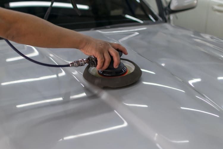 A person is polishing the hood of a car with an air sander.