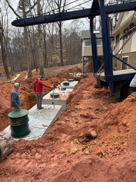 Workers install a precast concrete septic tank system in a backyard excavation next to a house. — Roxboro, NC — Premium Tanks & Stone Workers install a precast concrete septic tank system in a backyard excavation next to a house. — Roxboro, NC — Premium Tanks & Stone