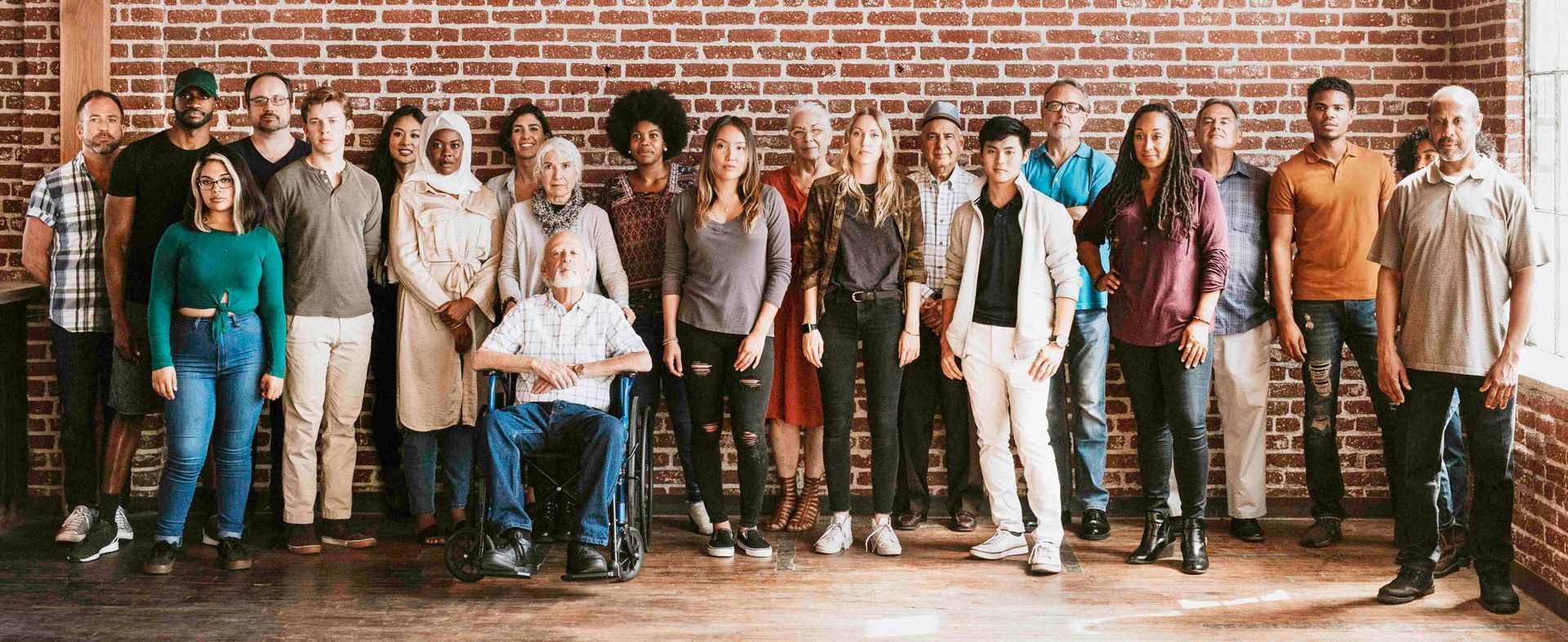 Group of people standing in front of a brick wall, diverse in attire, smiling, and looking at the camera.