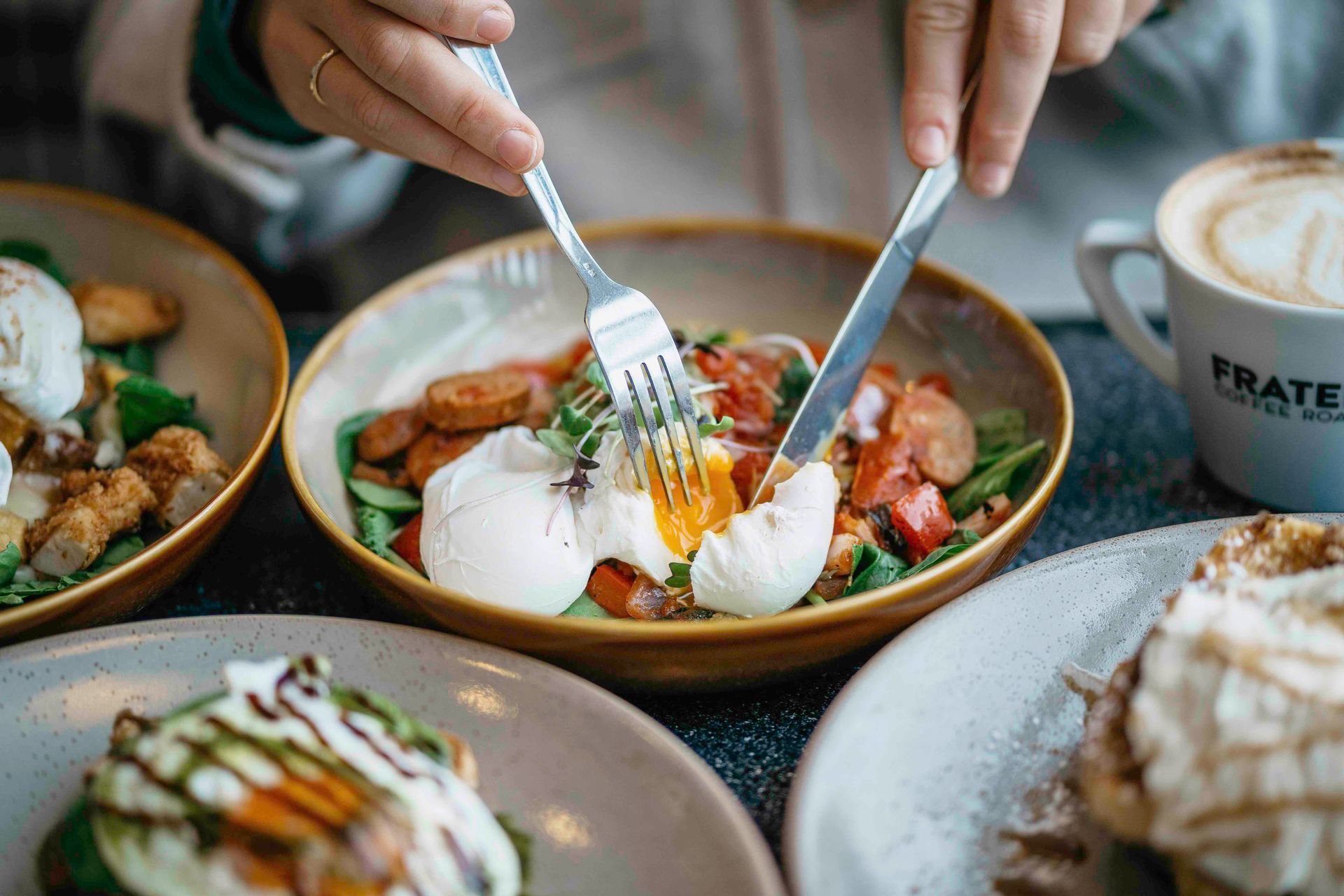 Person cutting into a poached egg with a fork and knife, alongside a salad in a bowl.