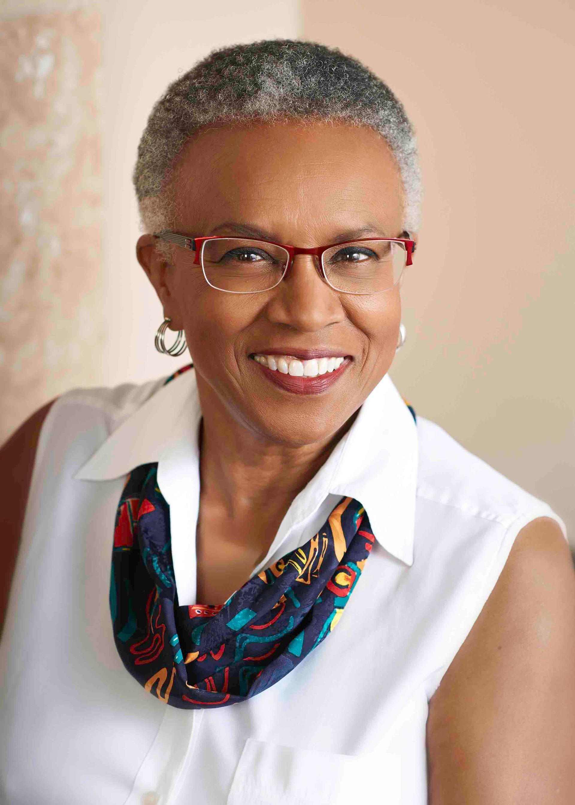 Woman in glasses, smiling, wearing a white shirt and patterned scarf.