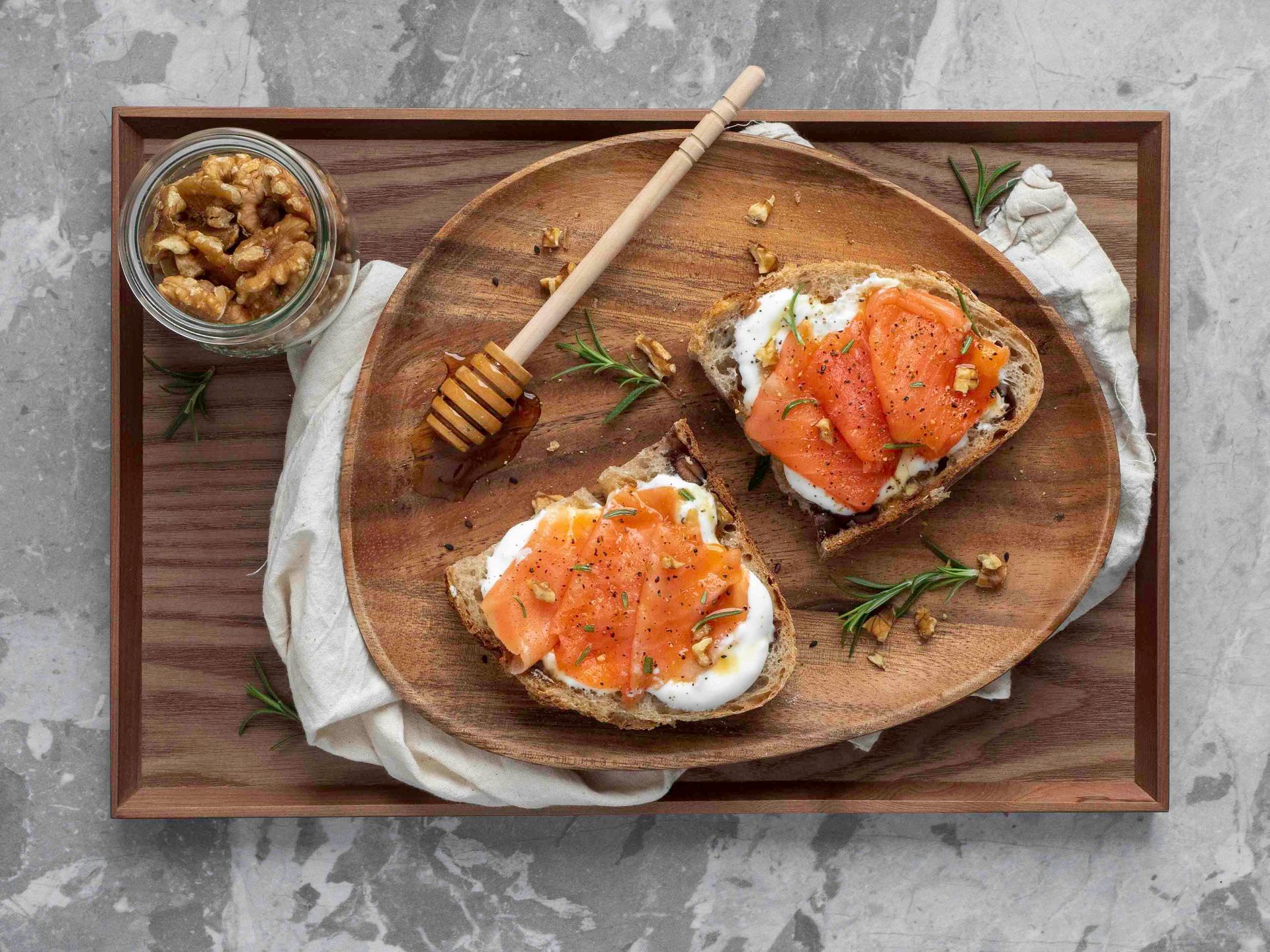 Toast with cream cheese and salmon on a wooden plate, walnuts, and honey.