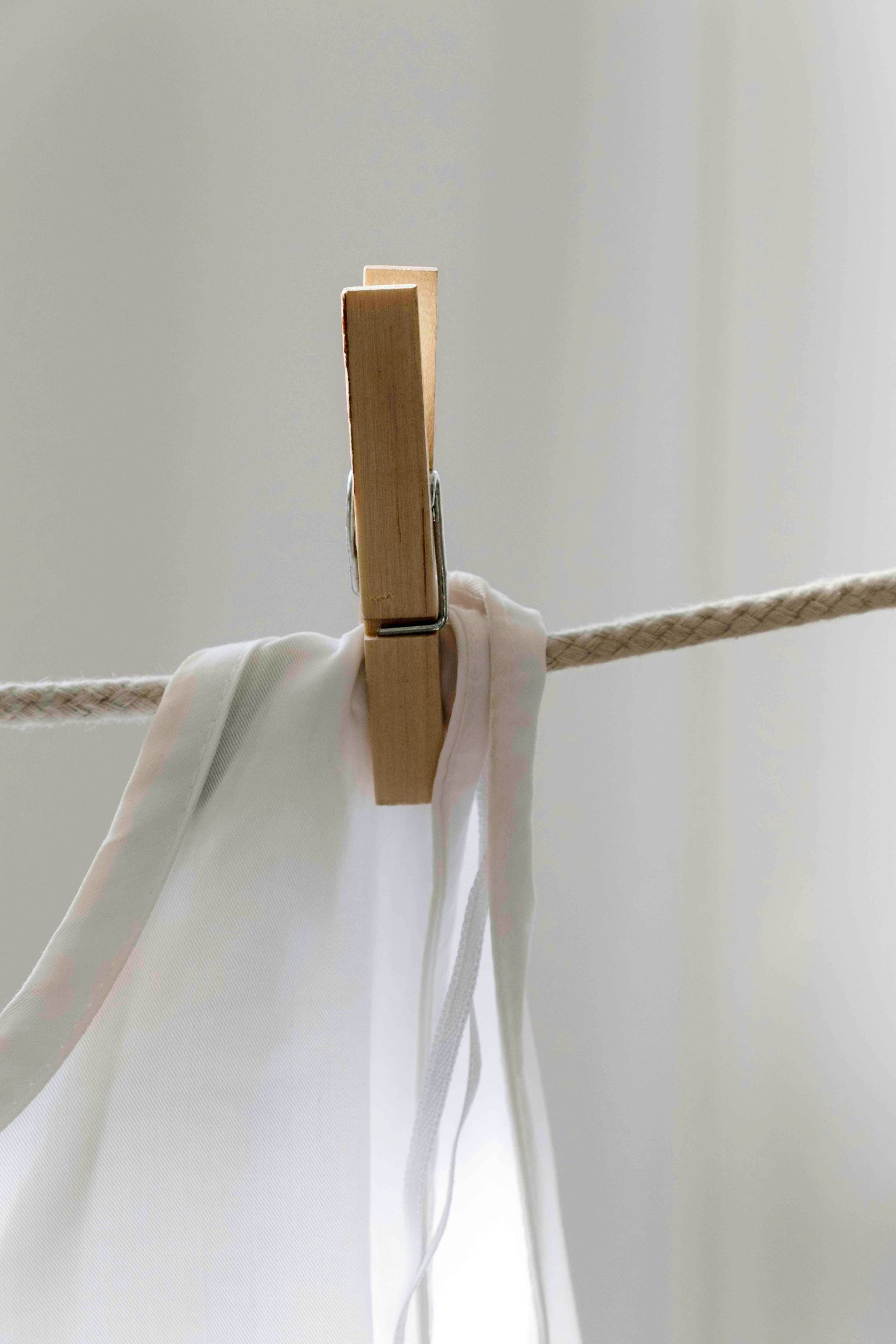 A wooden clothespin holds a sheer white fabric on a rope clothesline.