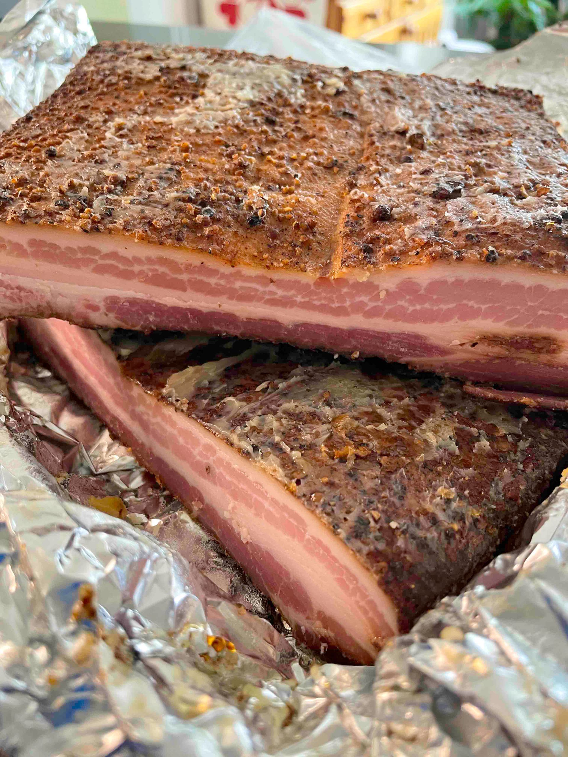 Smoked pork belly, cut, layered on foil, displaying pink and brown layered meat.