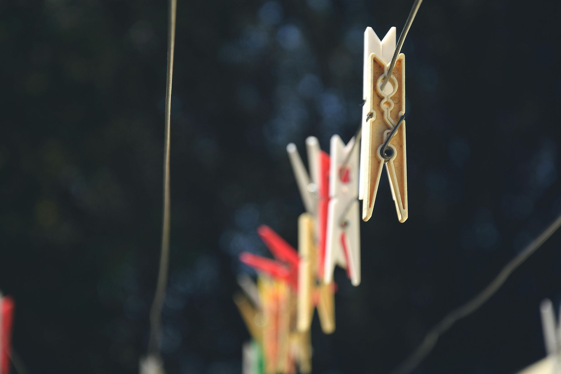 Clothes pins of various colors hanging on a clothesline, blurred dark background.
