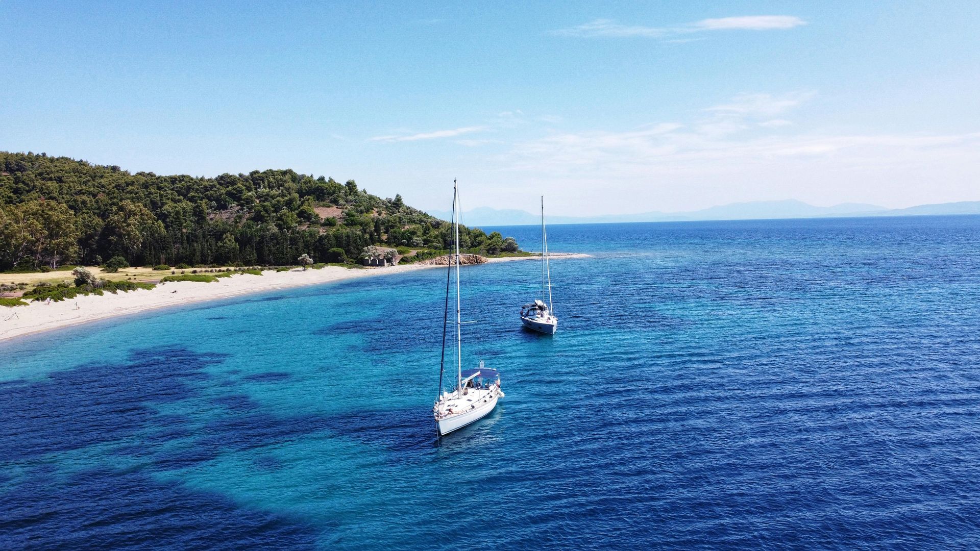Two sailboats anchored in turquoise water near a sandy beach.